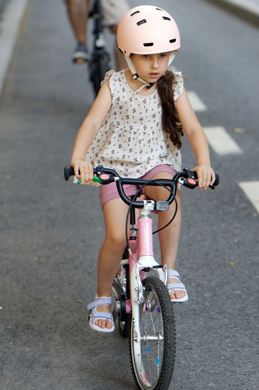 11 - Child riding a pink Woom children's bicycle, equipped with a matte pink helmet and pastel sandals